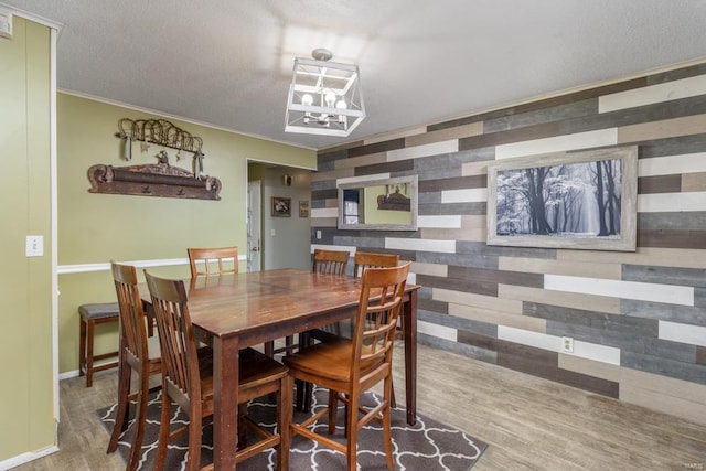 dining room featuring hardwood / wood-style floors, wooden walls, a textured ceiling, and ornamental molding