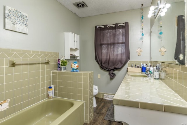 bathroom featuring vanity, a textured ceiling, wood-type flooring, toilet, and a bathing tub