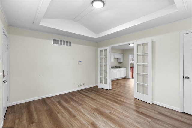 unfurnished room featuring french doors, light wood-type flooring, a tray ceiling, and ornamental molding