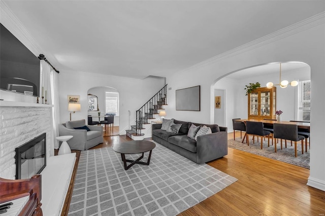 living room featuring a stone fireplace, ornamental molding, a chandelier, and hardwood / wood-style flooring