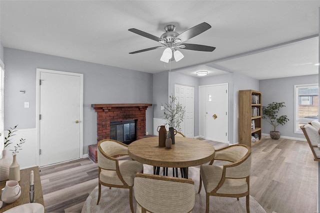 dining room featuring a brick fireplace, light hardwood / wood-style floors, and ceiling fan