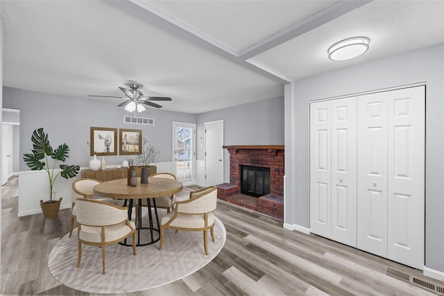 dining space with ceiling fan, a fireplace, and light wood-type flooring