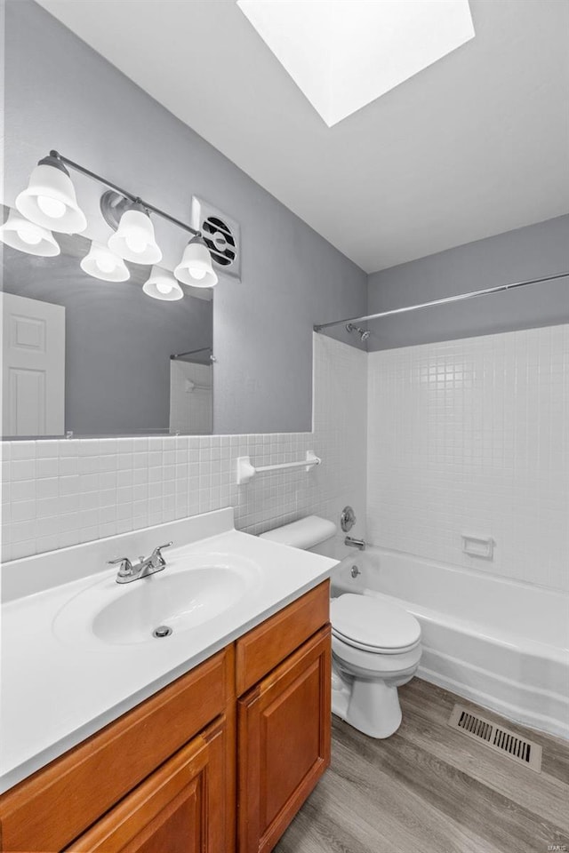 full bathroom with tiled shower / bath, a skylight, wood-type flooring, tile walls, and toilet