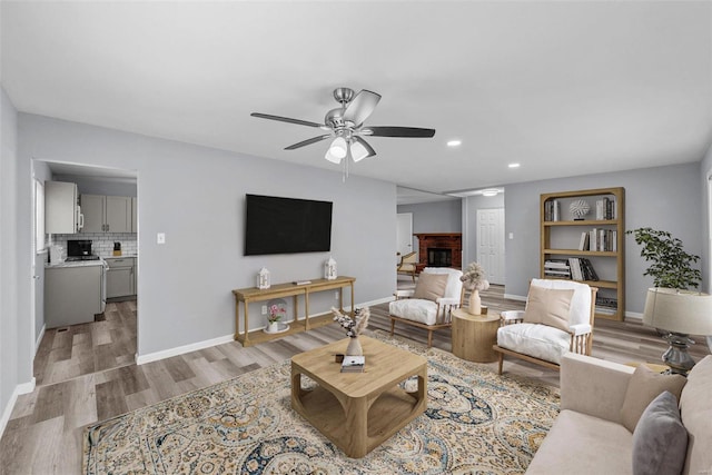 living room with ceiling fan, a fireplace, and light hardwood / wood-style floors