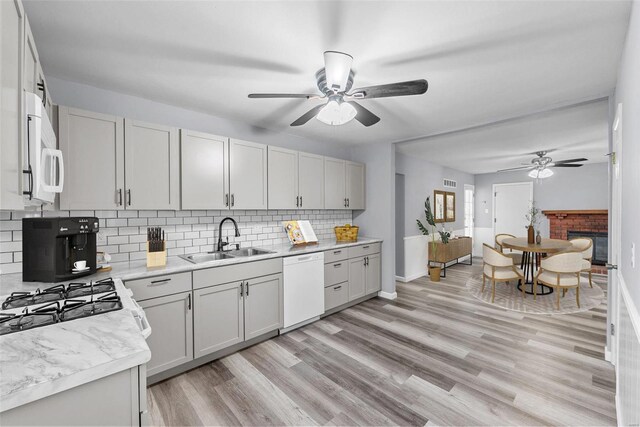 kitchen featuring a fireplace, sink, light wood-type flooring, backsplash, and white appliances