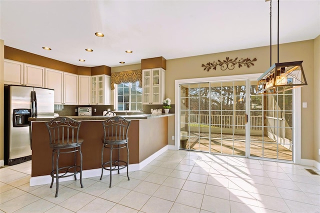 kitchen with a kitchen bar, stainless steel fridge, kitchen peninsula, light tile patterned floors, and hanging light fixtures