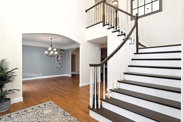 stairway featuring crown molding, wood-type flooring, and a notable chandelier