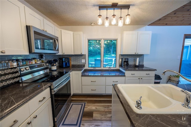 kitchen with appliances with stainless steel finishes, a textured ceiling, white cabinetry, and pendant lighting