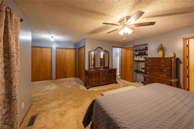 carpeted bedroom with multiple closets, ceiling fan, and a textured ceiling