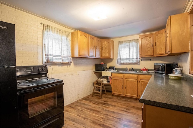 kitchen featuring sink, hardwood / wood-style flooring, black appliances, and brick wall