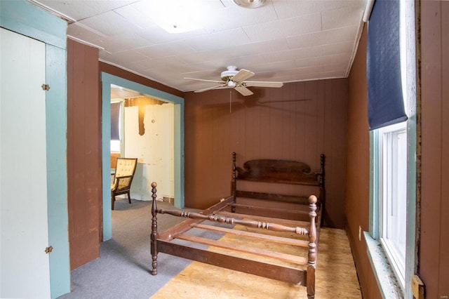 carpeted bedroom featuring ceiling fan and wood walls