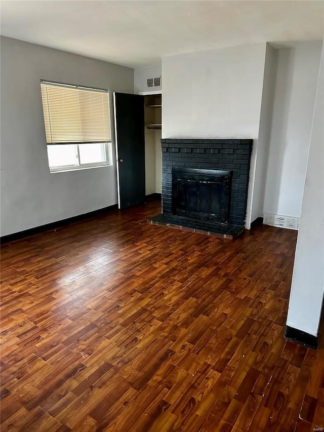 unfurnished living room featuring dark hardwood / wood-style flooring and a brick fireplace