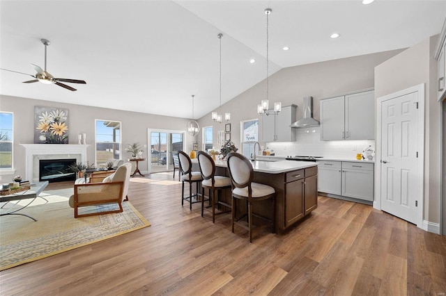 kitchen with sink, wall chimney range hood, a fireplace, an island with sink, and decorative light fixtures