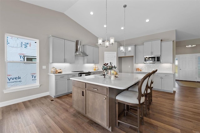 kitchen with pendant lighting, wall chimney range hood, a breakfast bar area, hardwood / wood-style floors, and a kitchen island