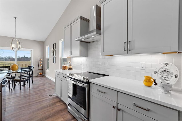 kitchen featuring gray cabinetry, tasteful backsplash, stainless steel appliances, hardwood / wood-style floors, and wall chimney range hood