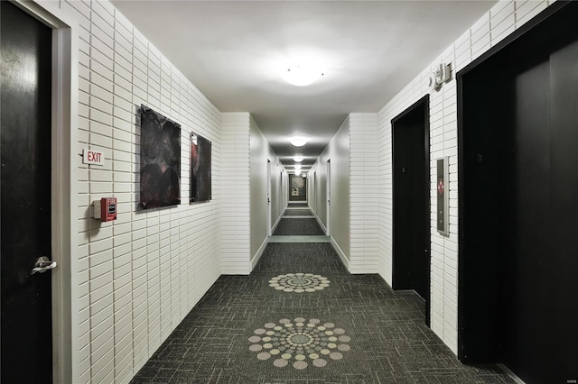 corridor with elevator, dark tile patterned floors, and tile walls