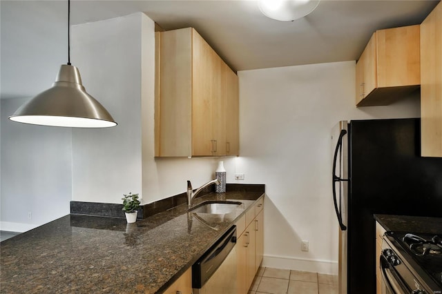 kitchen featuring dishwasher, sink, dark stone countertops, light brown cabinetry, and decorative light fixtures