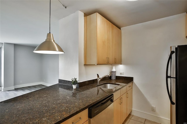 kitchen featuring black refrigerator, light brown cabinetry, stainless steel dishwasher, pendant lighting, and dark stone countertops