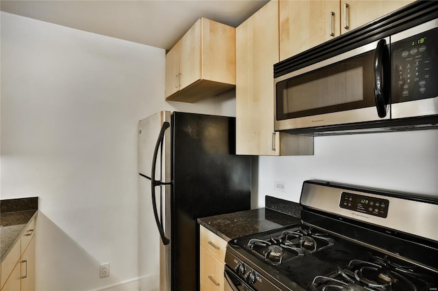 kitchen featuring light brown cabinets, black fridge, dark stone countertops, and range with gas stovetop