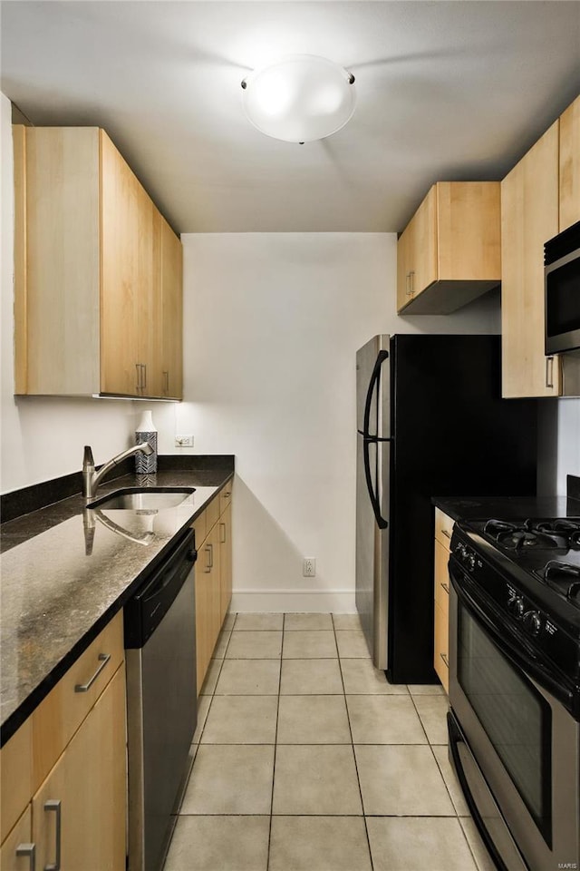 kitchen featuring appliances with stainless steel finishes, sink, light brown cabinets, light tile patterned floors, and dark stone countertops