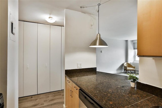 kitchen featuring stainless steel dishwasher, wood-type flooring, light brown cabinets, dark stone countertops, and hanging light fixtures