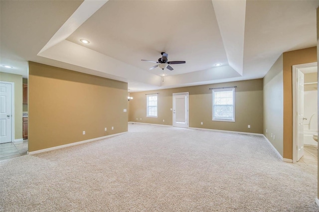 carpeted spare room featuring ceiling fan, a raised ceiling, and a wealth of natural light