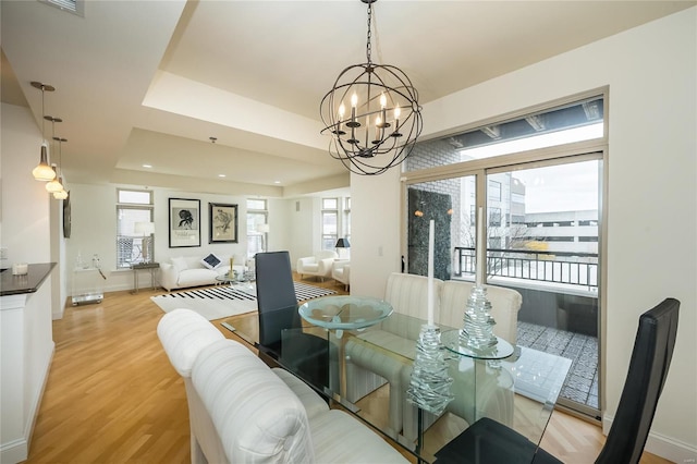 dining room featuring light wood-type flooring, a tray ceiling, and a notable chandelier