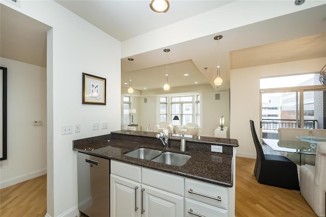 kitchen featuring decorative light fixtures, dark stone countertops, stainless steel dishwasher, white cabinets, and sink