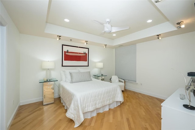 bedroom featuring ceiling fan, light hardwood / wood-style floors, and a tray ceiling