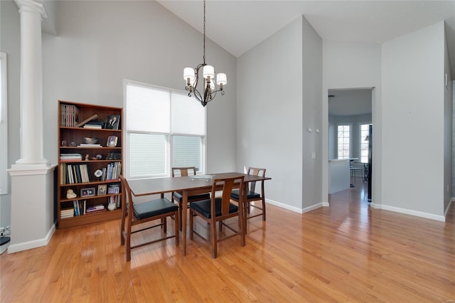 dining space featuring high vaulted ceiling, a notable chandelier, decorative columns, and light hardwood / wood-style floors