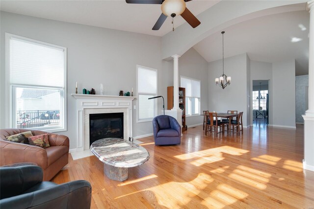 living room featuring decorative columns, lofted ceiling, ceiling fan with notable chandelier, and light wood-type flooring