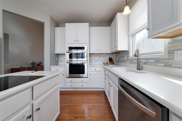 kitchen featuring pendant lighting, sink, white cabinetry, backsplash, and stainless steel appliances