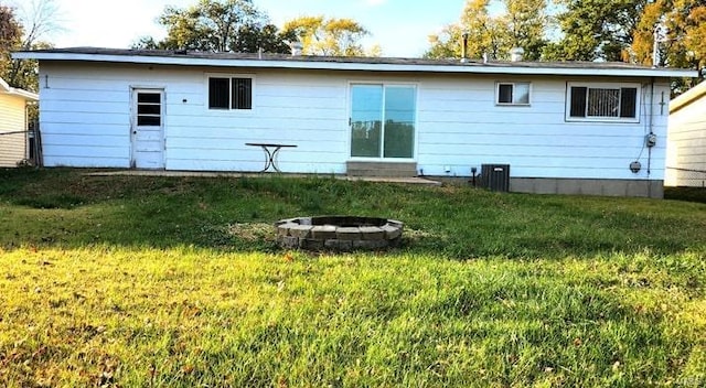 rear view of house with central AC, an outdoor fire pit, and a lawn