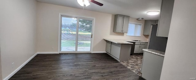 kitchen with gray cabinetry, dark hardwood / wood-style floors, stainless steel fridge, ceiling fan, and light stone counters