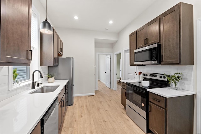 kitchen featuring sink, stainless steel appliances, pendant lighting, decorative backsplash, and light wood-type flooring