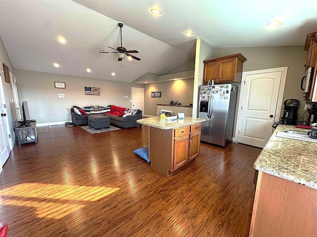 kitchen featuring stainless steel refrigerator with ice dispenser, dark hardwood / wood-style flooring, light stone counters, ceiling fan, and a kitchen island