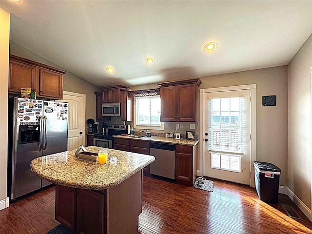 kitchen featuring a center island, sink, vaulted ceiling, appliances with stainless steel finishes, and light stone counters