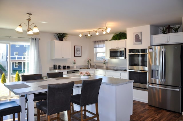 kitchen with white cabinetry, a center island, hanging light fixtures, a chandelier, and appliances with stainless steel finishes