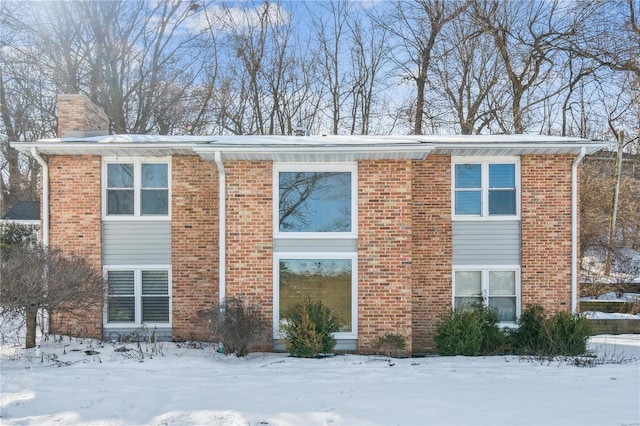 view of snowy exterior with brick siding and a chimney