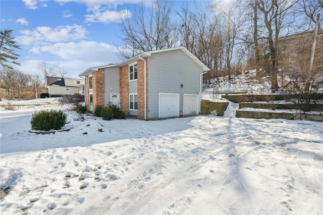 view of snowy exterior featuring a garage and brick siding