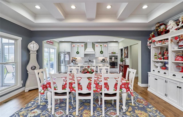 dining area with light hardwood / wood-style floors, coffered ceiling, beamed ceiling, and a healthy amount of sunlight