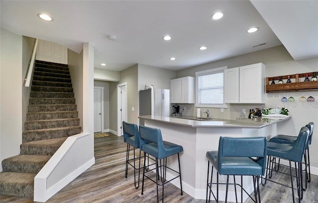 kitchen featuring white cabinetry, a kitchen breakfast bar, sink, kitchen peninsula, and stainless steel refrigerator