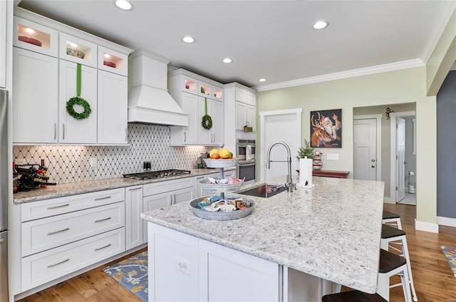 kitchen with custom exhaust hood, an island with sink, stainless steel appliances, a kitchen breakfast bar, and white cabinets