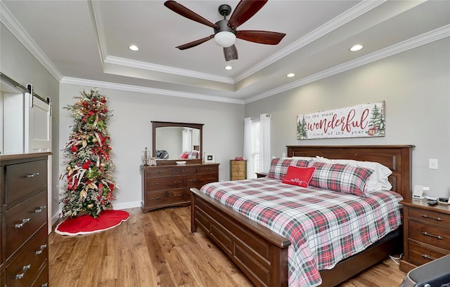 bedroom with a barn door, light hardwood / wood-style floors, ceiling fan, a tray ceiling, and crown molding