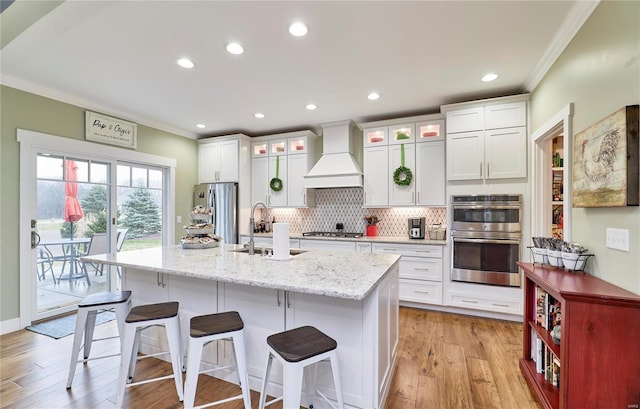 kitchen featuring crown molding, a center island with sink, stainless steel appliances, and premium range hood