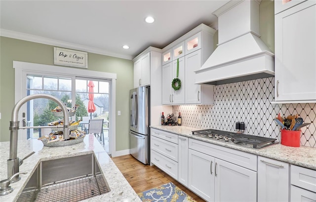 kitchen featuring premium range hood, sink, white cabinets, ornamental molding, and stainless steel appliances