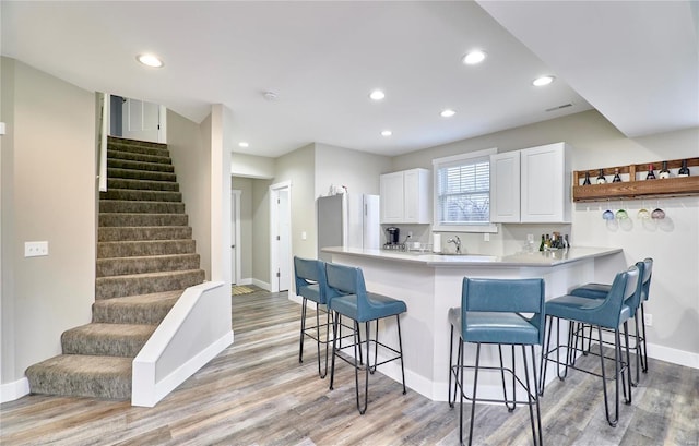 kitchen with stainless steel refrigerator, white cabinets, a kitchen breakfast bar, kitchen peninsula, and light wood-type flooring