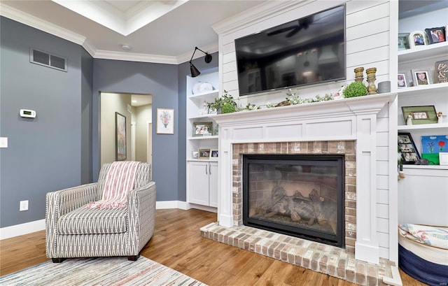 sitting room featuring light hardwood / wood-style flooring, a raised ceiling, crown molding, a brick fireplace, and built in shelves