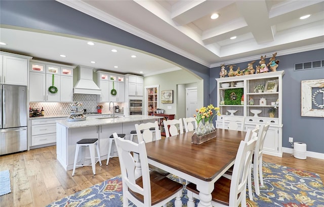 dining area featuring crown molding, sink, beam ceiling, and light hardwood / wood-style flooring