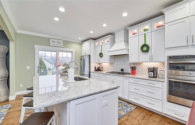 kitchen featuring white cabinetry, stainless steel appliances, custom range hood, and a center island with sink